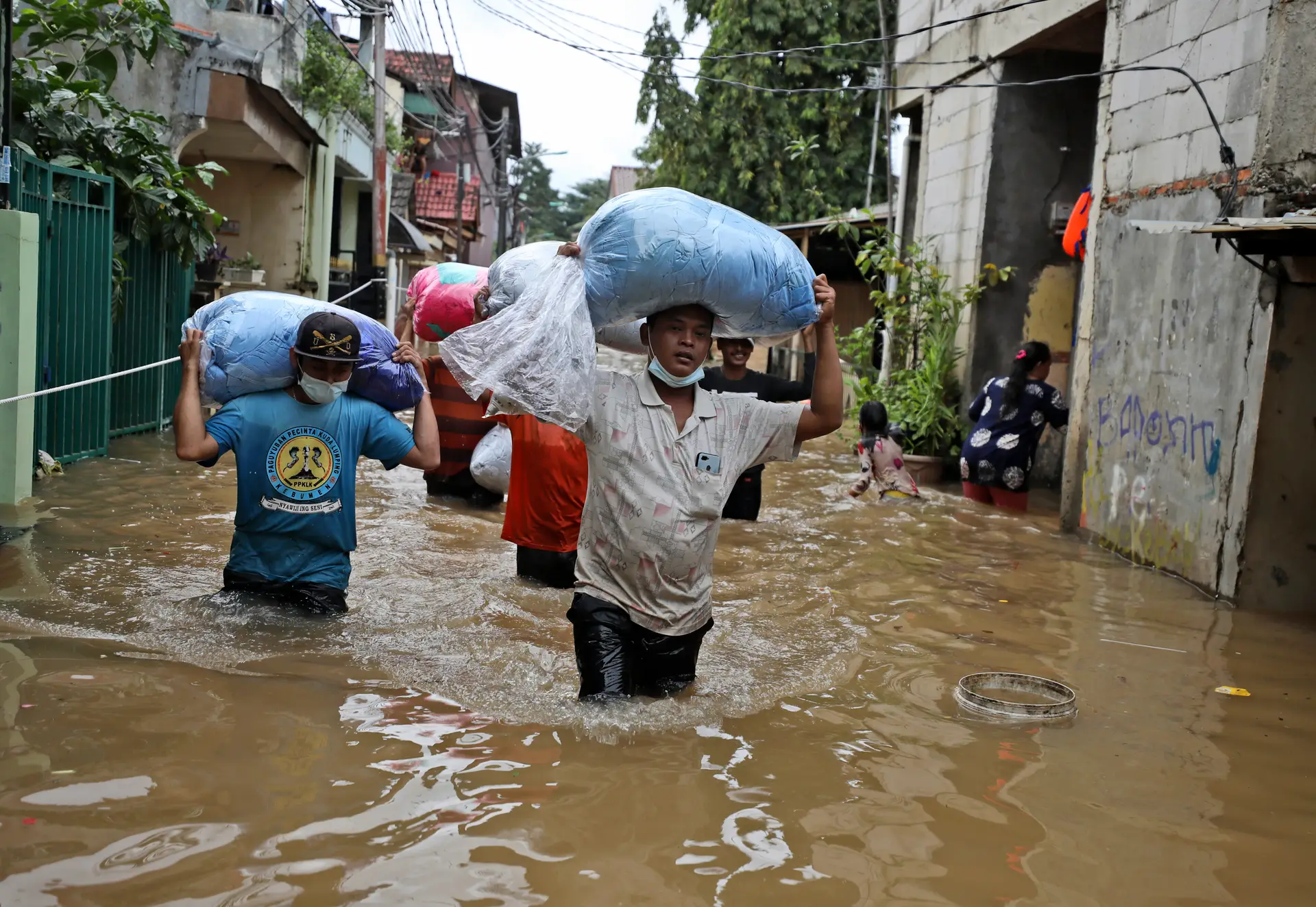 Indonésios carregam os seus pertences à medida que caminham sobre a água num bairro inundado após fortes chuvas em Jacarta, Indonésia  