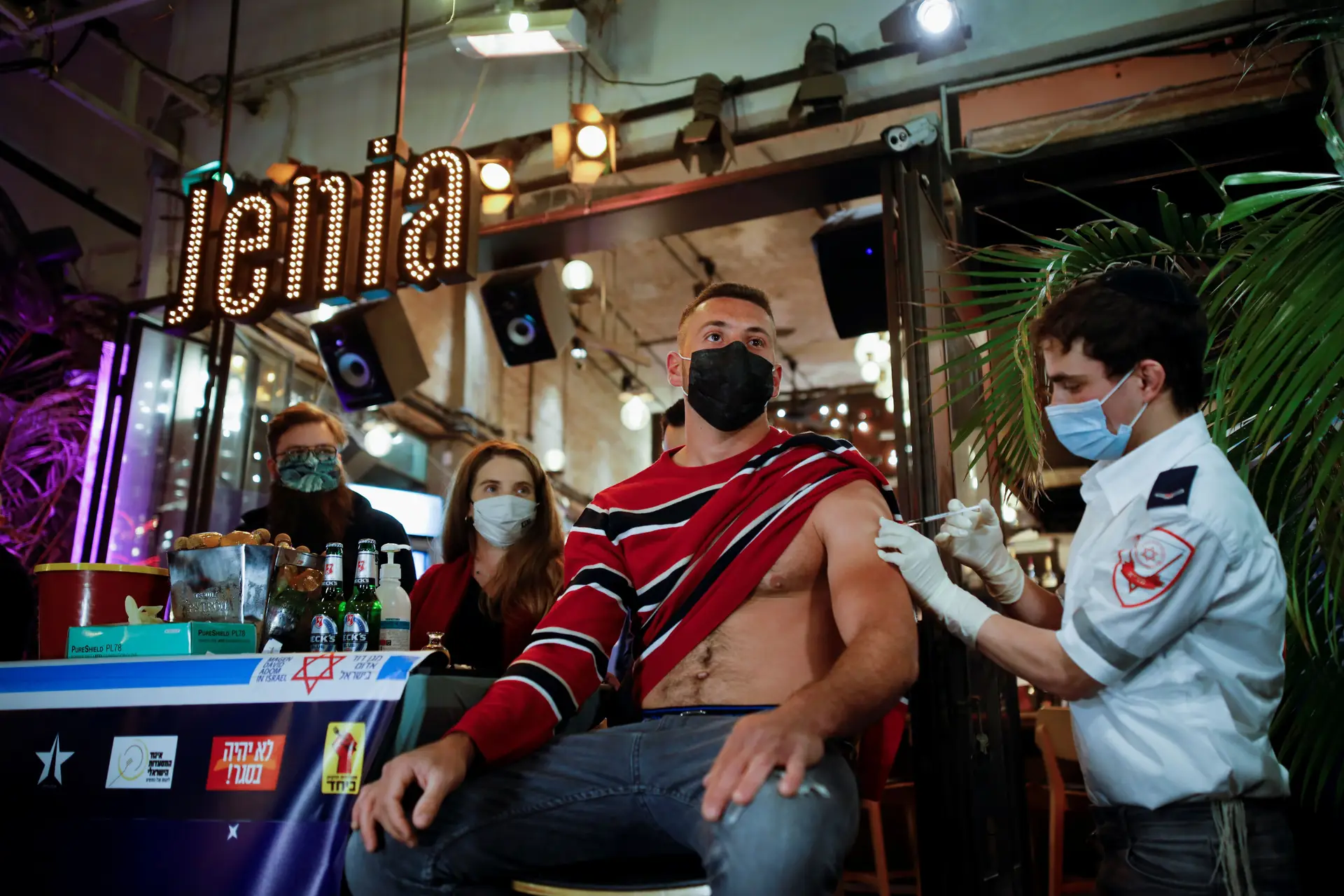 Um homem recebe uma dose da vacina contra a covid-19, como parte de uma iniciativa do município de Tel Aviv, que oferece uma bebida grátis num bar aos residentes que tomem a vacina. Tel Aviv, Israel.