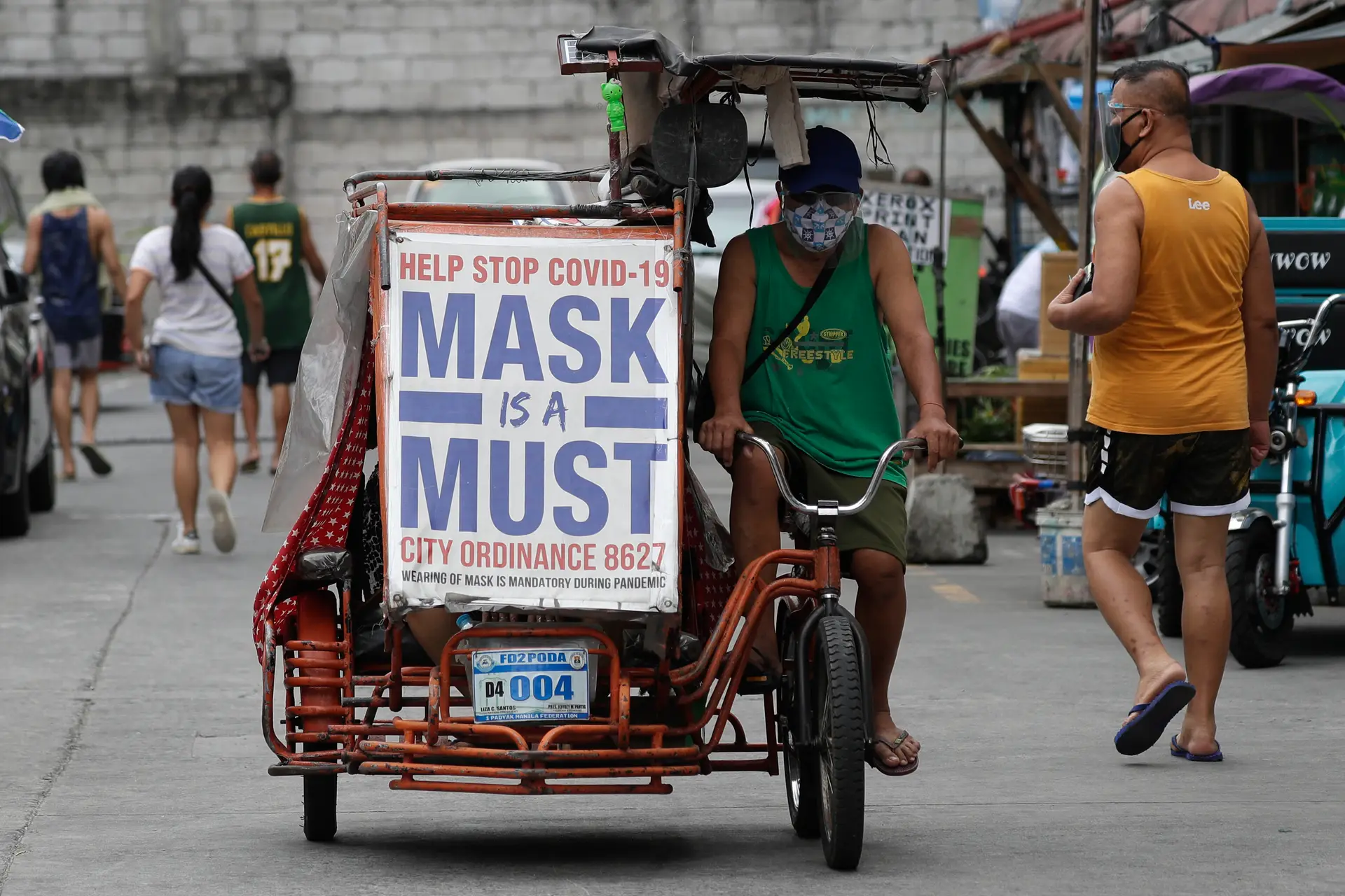Um homem conduz o seu "Pedi Cab" (também conhecido como "eco táxi"), que tem um cartaz que recorda a importância do uso de máscara para evitar a propagação do novo coronavírus, em Manila, nas Filipinas.