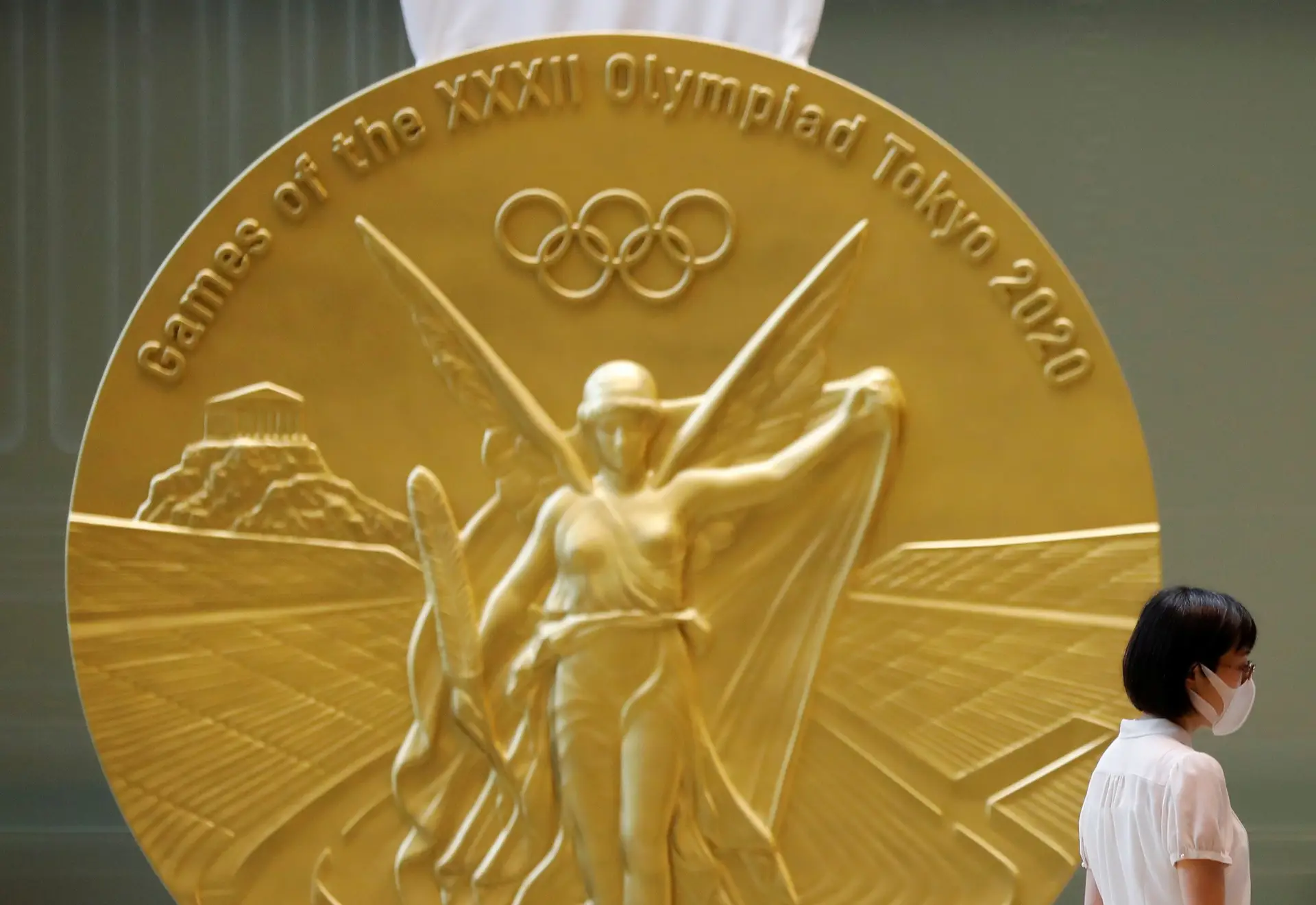 Mulher a usar máscara passa por uma reprodução em grande escala da medalha dos Jogos Olímpicos de Tóquio 2020 na Torre Nihonbashi Mitsui em Tóquio, Japão.
