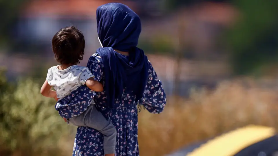 Cidadão afegã com um bebé ao colo no campo de refugiados da Cruz Vermelha, em Itália.