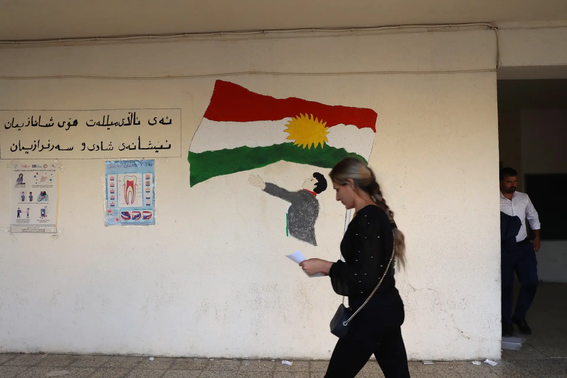 Uma eleitora iraquiana passa por um desenho da bandeira do Curdistão após votar durante um dia especial de votação para a eleição parlamentar legislativa iraquiana em Erbil, capital da região do Curdistão no Iraque. 