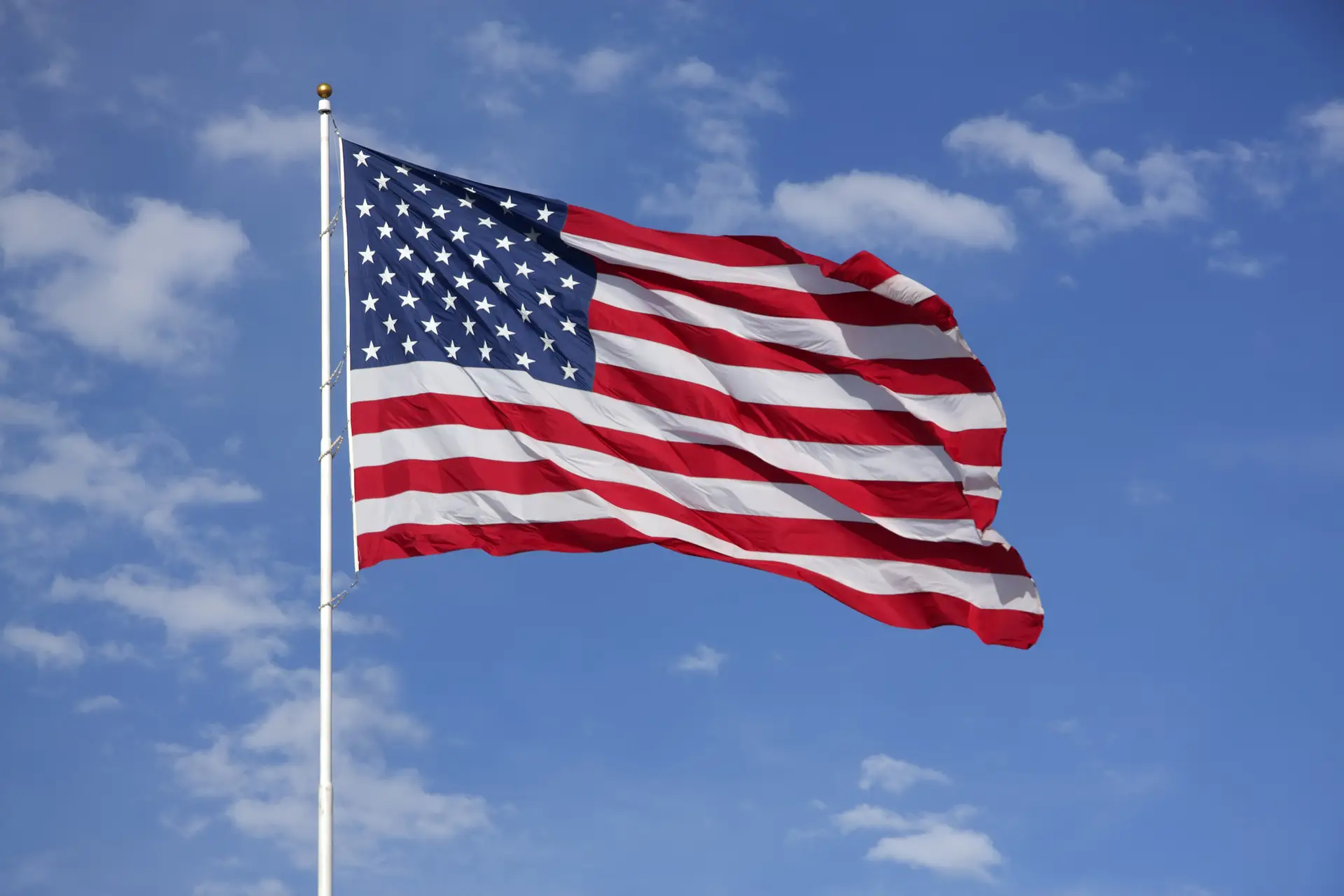 Full American Flag flying in the wind, with blue sky and clouds behind it