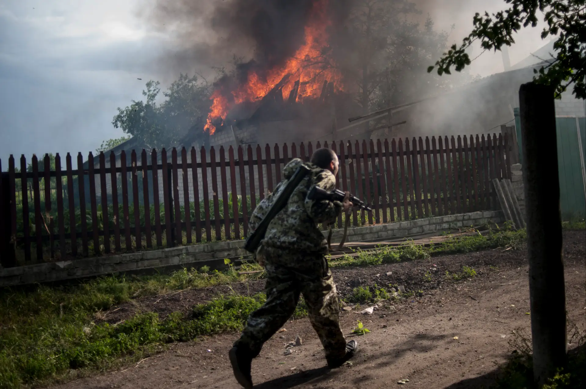 A pro-Russian armed man runs past a burning house after it was set on fire by a mortar shell, on the outskirts of the town of Lysychansk, Ukraine, on Thursday, May 22, 2014. In the eastern Luhansk region, sustained gunfire and shelling rocked the town of Lysychansk. One mortar bomb hit a house, which burst into flames. Earlier today at least 11 Ukrainian troops were killed and about 30 others were wounded during an attack at a military checkpoint, the deadliest raid in the weeks of fighting in eastern Ukraine. (AP Photo/Evgeniy Maloletka)
