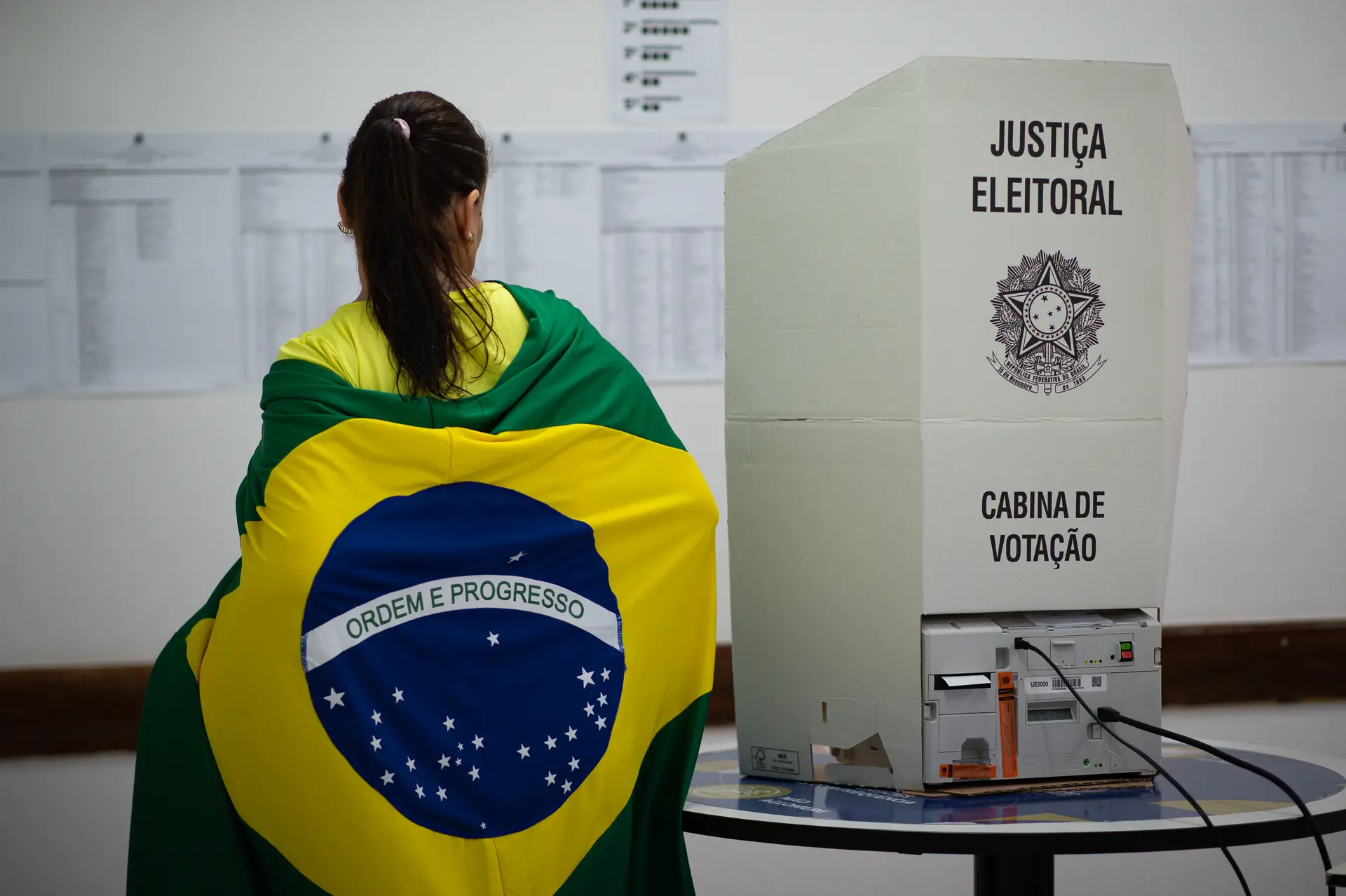 Mulher com bandeira brasileira nas costas vota nas eleições do Brasil.