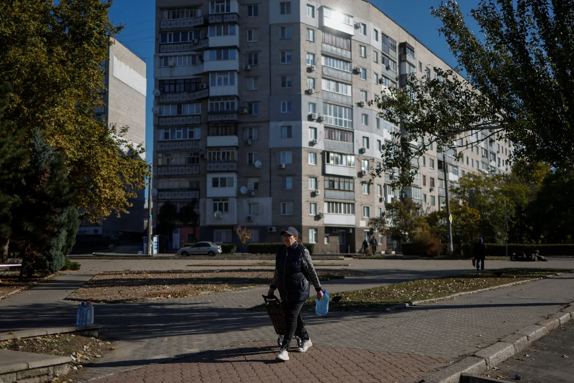 Mulher caminha pela rua com garrafões cheios de água fresca na região de Kherson.