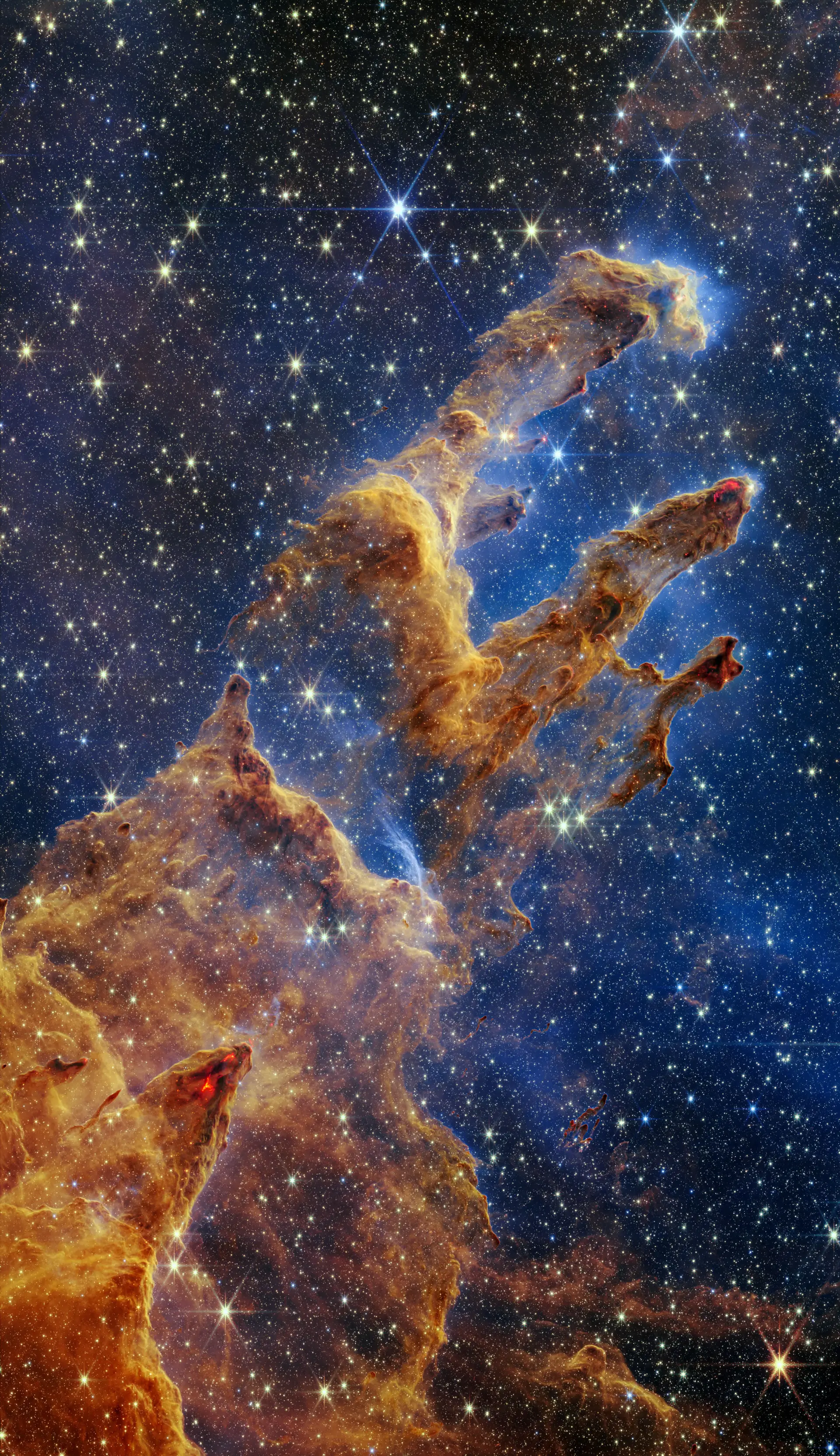 Os "Pilares da Criação" na visão de luz infravermelha do Telescópio Espacial James Webb. Parecem arcos e pináculos a sair de uma paisagem desértica, mas estão cheios de gás e poeiras semitransparentes. É uma região onde estrelas se estão a formar.