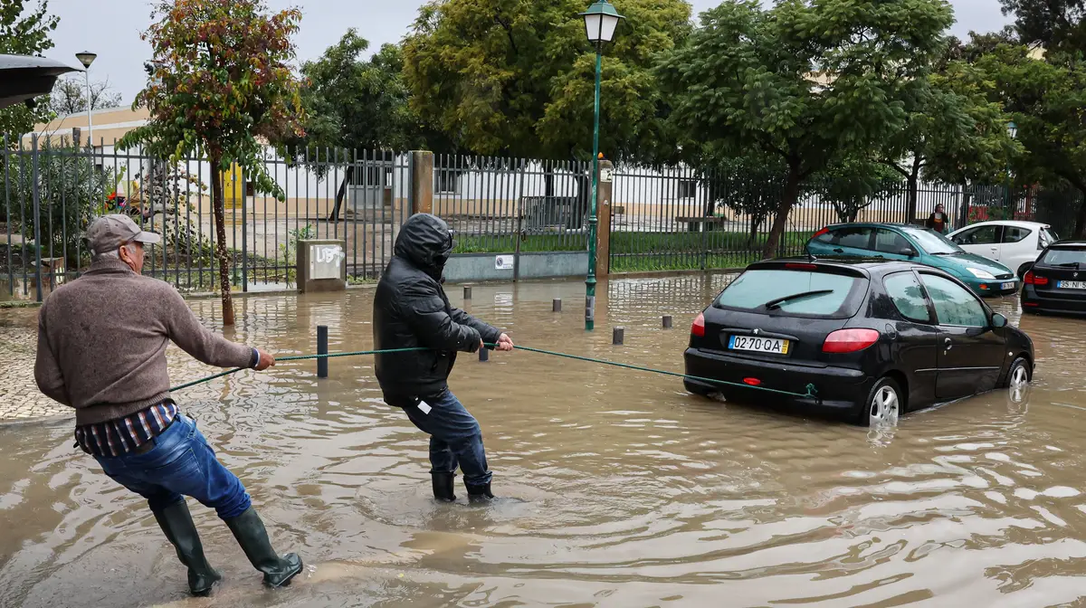 Populares tentam retirar um veículo de uma rua inundada após a chuva forte ter alagado a baixa de Faro.