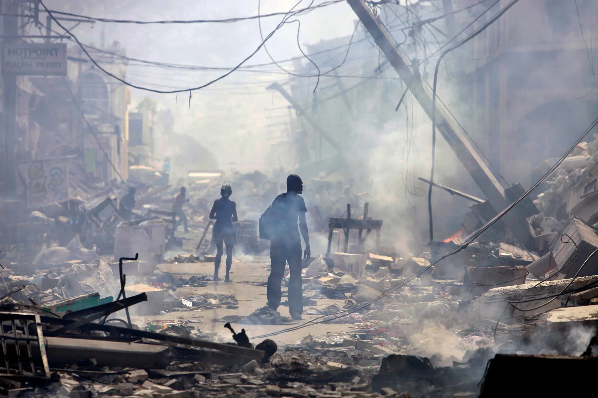 Pessoas caminham por uma rua com vários edifícios a arder em Port-au-Prince, no Haiti, em 2010.