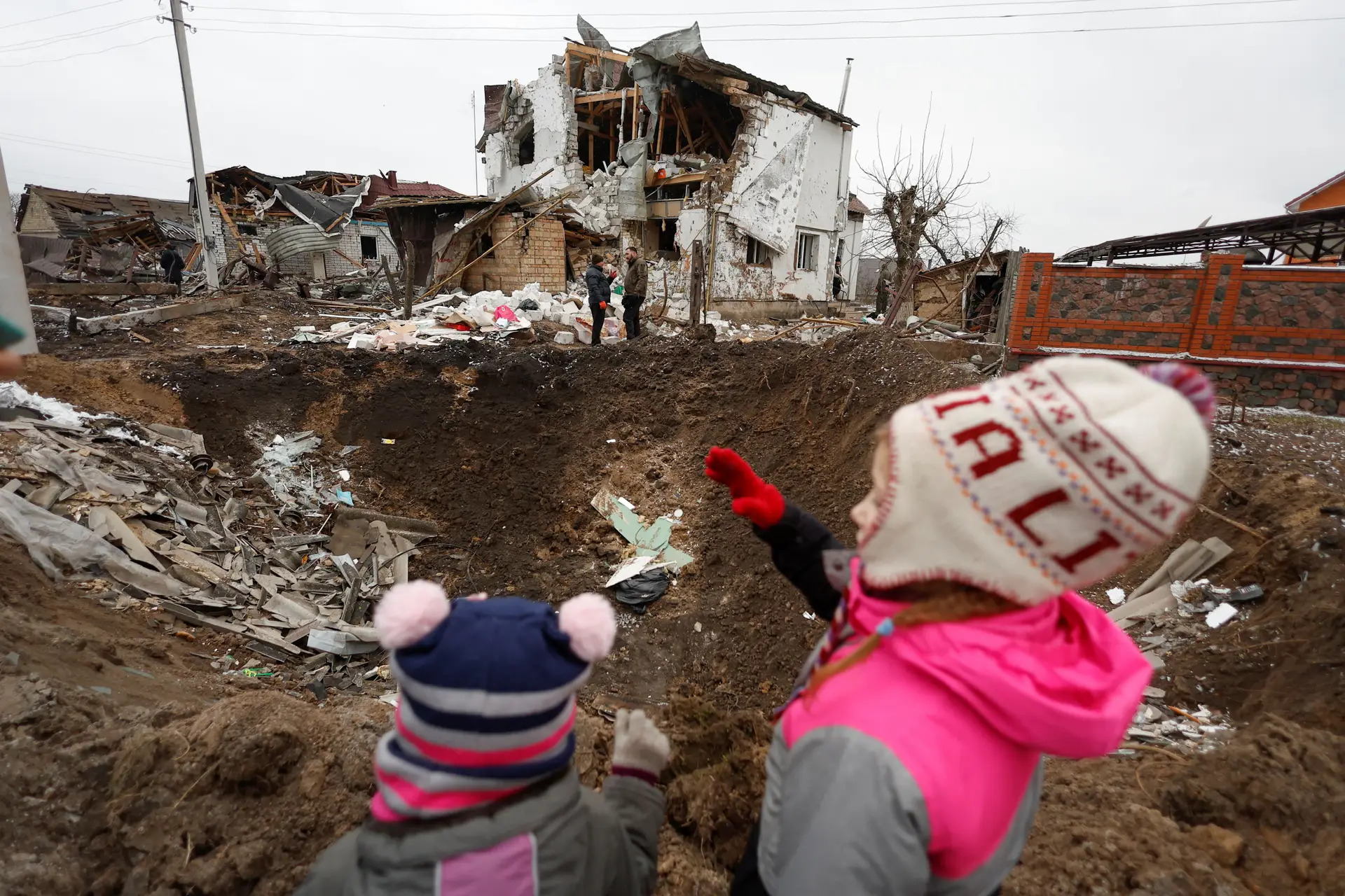 Crianças ao lado de uma cratera deixada por um ataque militar russo, na cidade de Hlevakha, nos arredores de Kiev.
