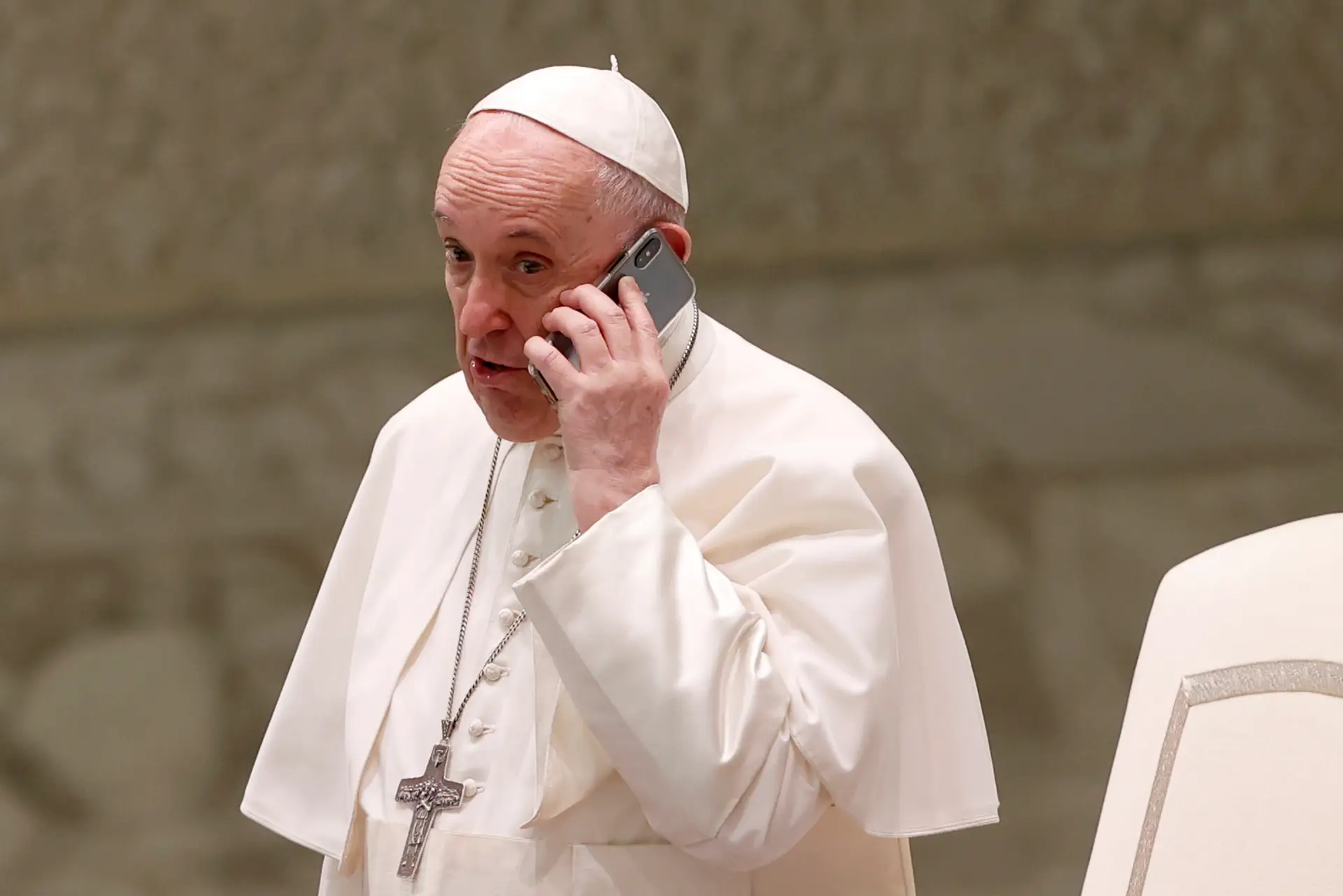 O Papa fala ao telefone, dado pelo seu assessor, Piergiorgio Zanetti, no final da audiência semanal na sala Paulo VI no Vaticano, 11 de agosto de 2021