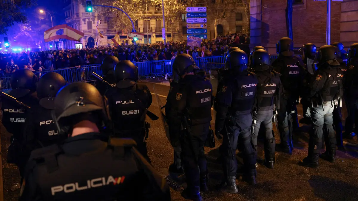 Polícias de choque montam guarda enquanto as pessoas participam num protesto perto da sede do Partido Socialista Espanhol (PSOE)