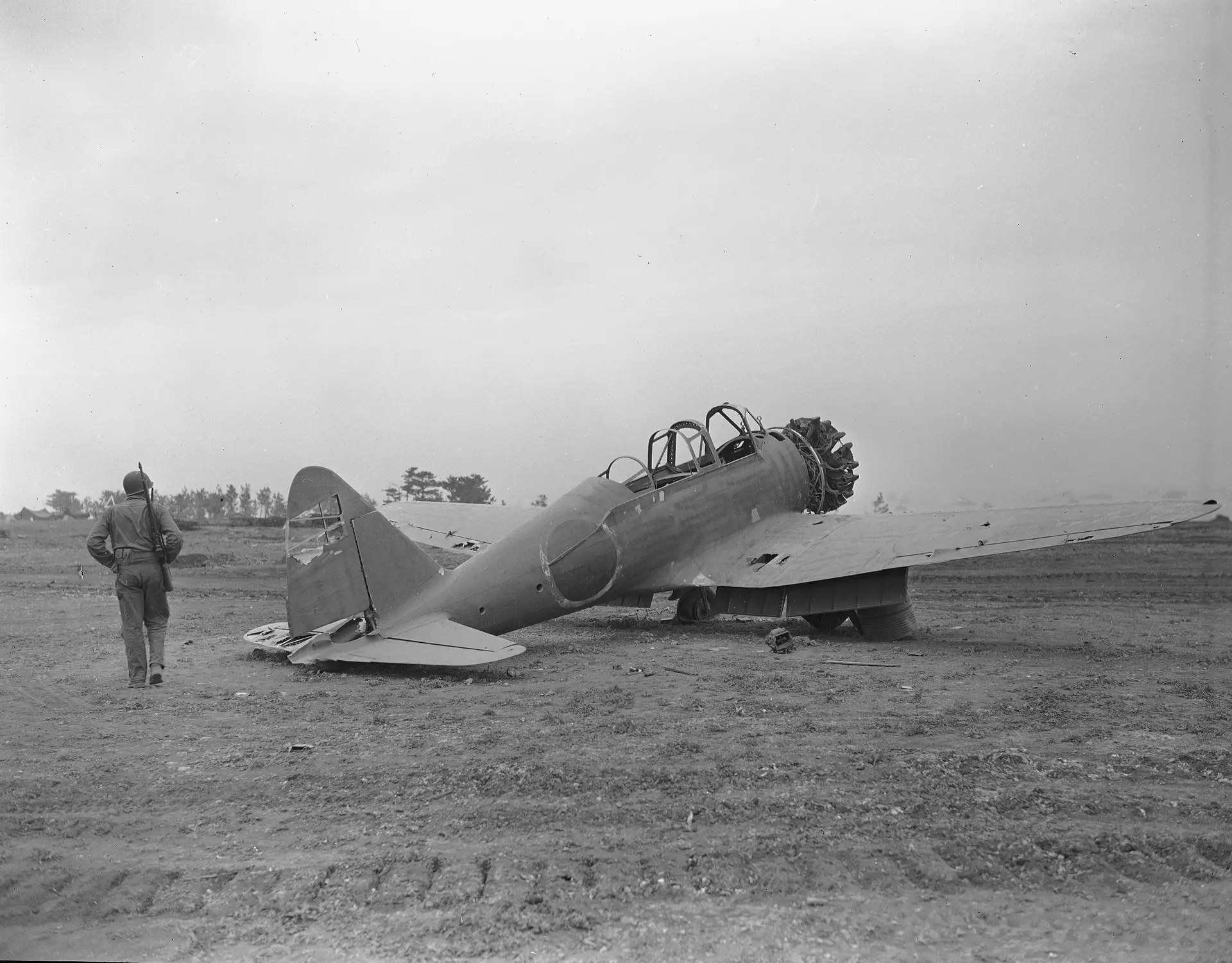Um soldado norte-americano inspeciona um avião de combate japonês danificado no campo de aviação de Okinawa, a 16 de abril de 1945.