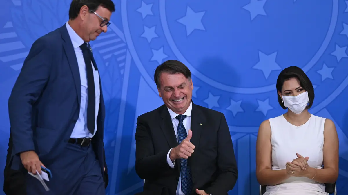 O presidente do Brasil, Jair Bolsonaro (centro), ao lado do ministro do Turismo do Brasil, Gilson Machado (à esquerda) e da primeira-dama Michelle Bolsonaro (à direita), reage durante a cerimónia de posse do ministro do Turismo do Brasil, Gilson Machado, em meio à pandemia do Coronavírus (COVID - 19) no Palácio do Planalto em 17 de dezembro de 2020 em Brasília.
