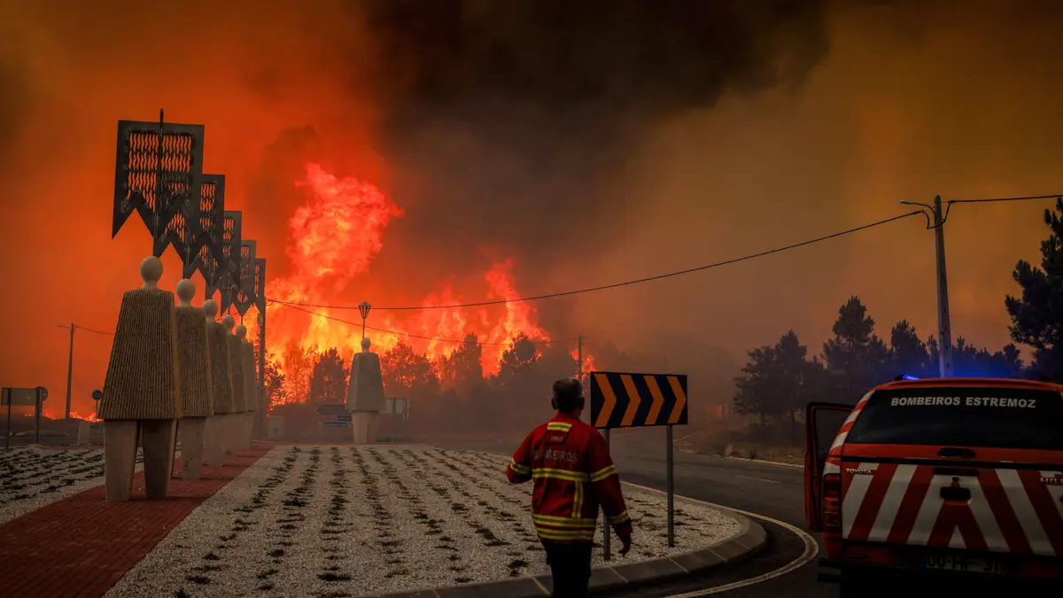 Um membro de uma corporação de bombeiros voluntários caminha enquanto um incêndio florestal avança em Lamosa, no concelho de Sernancelhe, distrito de Viseu, Portugal, a 14 de agosto de 2025.