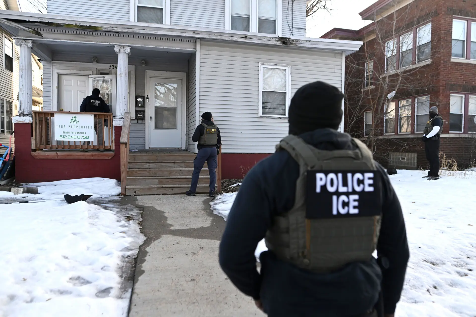 Agentes do Serviço de Imigração e Alfândega dos Estados Unidos (ICE) aproximam‑se de uma casa antes de deter duas pessoas em 13 de janeiro de 2026, na cidade de Minneapolis, no estado de Minnesota, como parte de uma grande operação de fiscalização da imigração liderada pelo governo federal.
