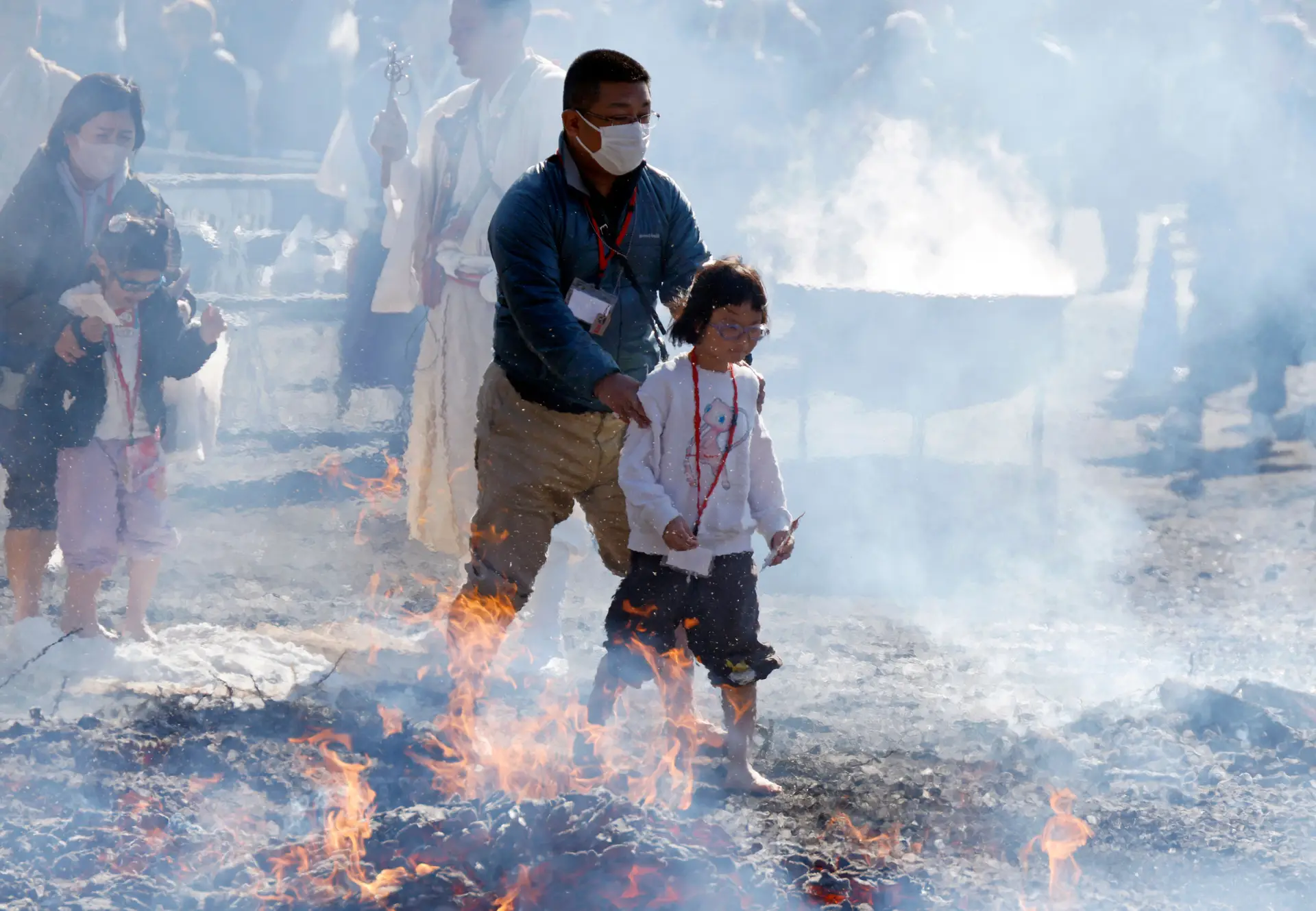 Homem e criança caminham descalços sobre as brasas